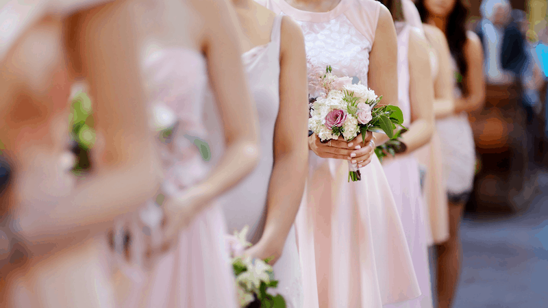 Bridesmaids in soft pink dresses standing in line, each holding small bouquets with white and blush flowers
