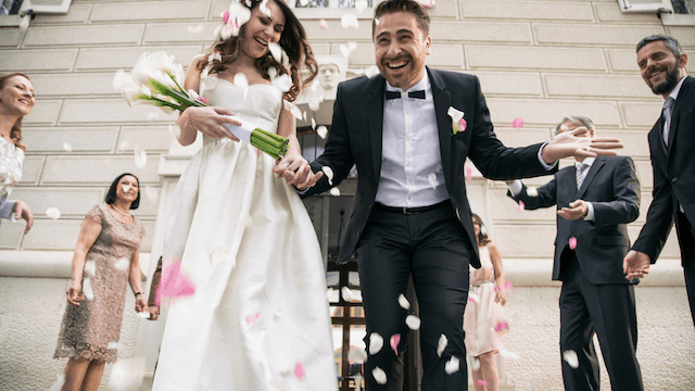 Who Is In A Wedding Party? 11 Joyful bride and groom exit their wedding ceremony hand in hand, smiling and laughing as guests shower them with rose petals