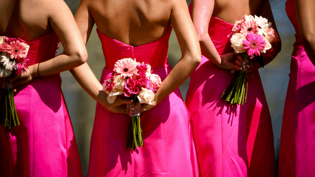 Bridesmaids in bright pink strapless dresses holding bouquets of pink and white flowers behind their backs