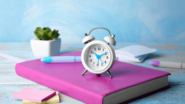 Why Does Wedding Planning Take So Long? 2 a pink notebook with an alarm clock sitting on it to symbolize Why does wedding planning take so long