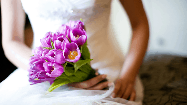 Bride holding purple flower bouquet.