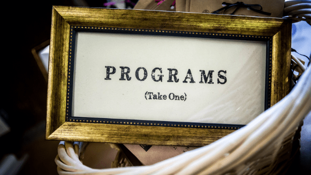 Wedding Planner Vs. Coordinator (Explained) 4 A sign saying "programs, take one" in a Basket with programs for guests.