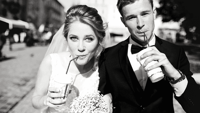 Bride and groom sipping drinks with straws, smiling in a candid black-and-white wedding photo