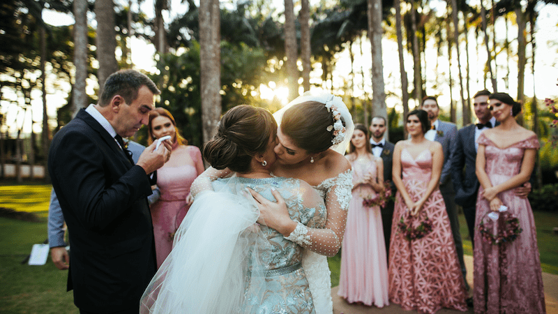 Mother Of The Bride Duties And Responsibilities 3 Bride embraces and kisses her mother during an outdoor wedding ceremony, with emotional guests and bridesmaids looking on.
