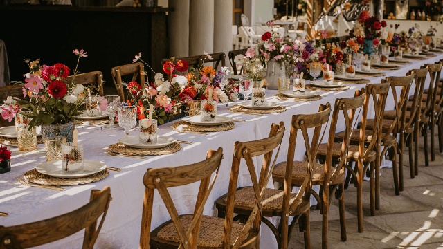 Wedding Ceremony And Reception In The Same Place? 2 Long wedding reception table with rustic wooden chairs, white linens, and vibrant floral centerpieces