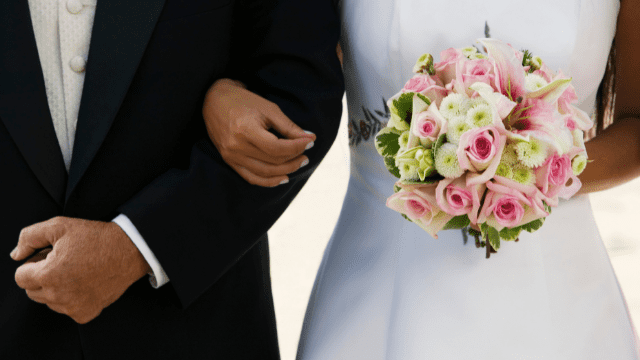 How to Deal With Parents Controlling Wedding Planning 2 bride holding a pink and white bouquet while walking arm-in-arm with a man in a black suit