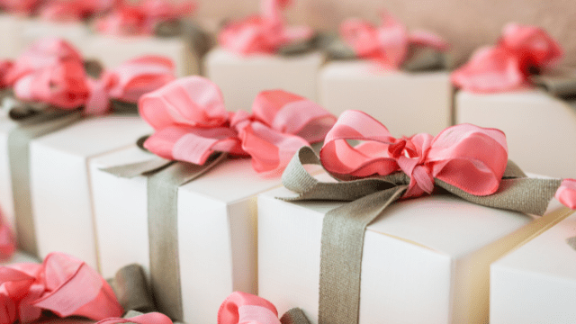 17 Hidden Wedding Costs You May Not Have Anticipated 3 Elegant white wedding favor boxes tied with pink and gray ribbons are arranged neatly on a table.
