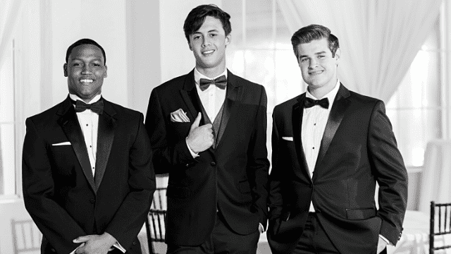Everything You Need to Know About Junior Groomsmen (But Were Afraid To Ask) 3 Three young groomsmen in tuxedos and bow ties pose for a black-and-white indoor wedding portrait
