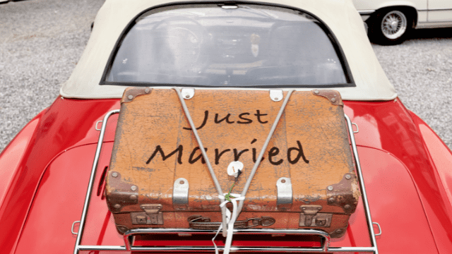 Post-Wedding Depression: When The Blues Set In after the Big Day 3 Vintage suitcase painted “Just Married” strapped to the luggage rack of a red convertible getaway car.