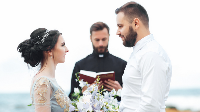 A couple exchanging vows during an outdoor ceremony, with an officiant in the background leading the service