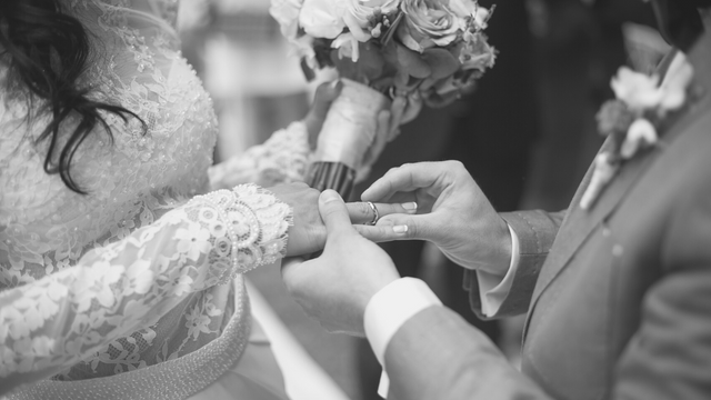 A bride and groom exchanging wedding rings during their ceremony, with the bride holding a bouquet of flowers