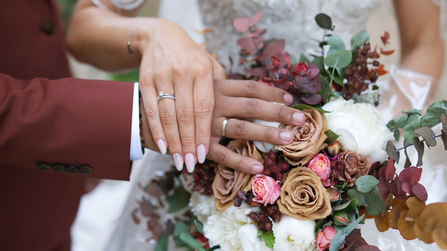 What Hand Does a Wedding Ring Go On? The Ultimate Guide 2 Bride in blush pink lace dress with high neckline and pearl earrings, hands near face showing engagement ring in soft light.