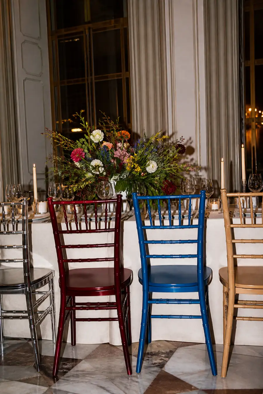 33 Jaw-Dropping Ways to Wow Your Wedding Guests at the Reception 15 Silver, oxblood, cobalt and natural wood chairs surround a candlelit wedding table topped with a colorful floral centerpiece.