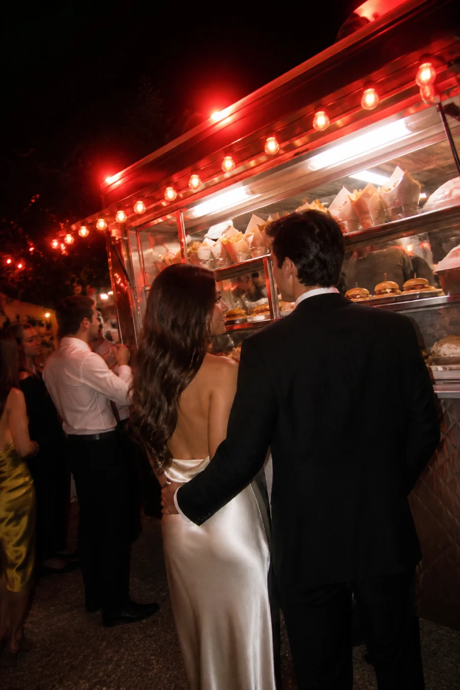 33 Jaw-Dropping Ways to Wow Your Wedding Guests at the Reception 7 Newlyweds wait beside a silver late-night food truck serving fries and sliders under vivid ruby lights after their reception.