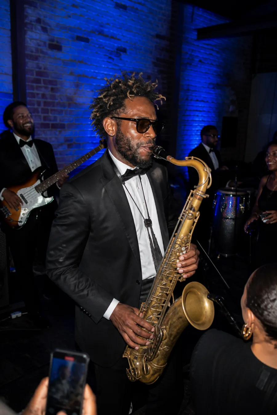 33 Jaw-Dropping Ways to Wow Your Wedding Guests at the Reception 16 Saxophonist performs with a live band under cobalt lighting as wedding guests gather close to the stage inside the reception