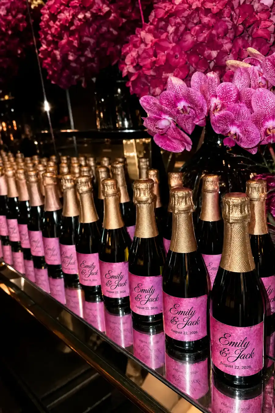 33 Jaw-Dropping Ways to Wow Your Wedding Guests at the Reception 5 Personalized champagne bottles with pink labels and gold lettering beside vibrant magenta wedding flowers