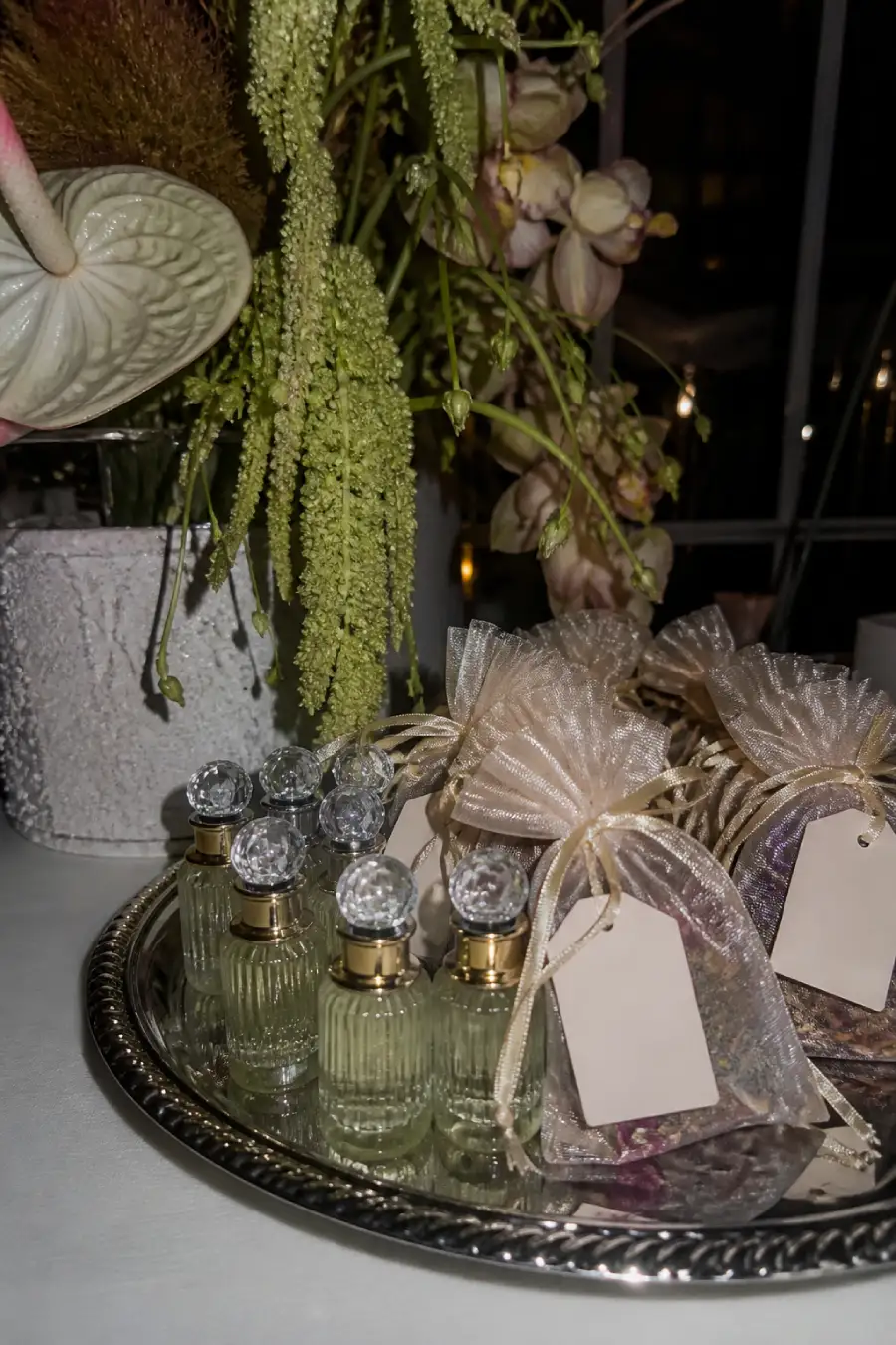 33 Jaw-Dropping Ways to Wow Your Wedding Guests at the Reception 13 Elegant glossy perfume bottles and translucent scent sachets rest on a silver tray beneath sculptural wedding flowers nearby