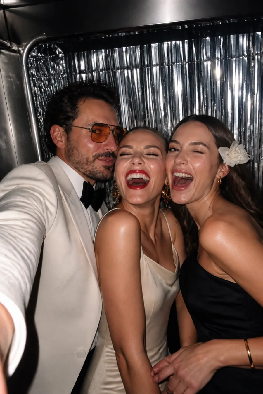 33 Jaw-Dropping Ways to Wow Your Wedding Guests at the Reception 2 Three fashionable wedding guests laugh together inside the silver-fringed photo booth while posing for a direct-flash selfie