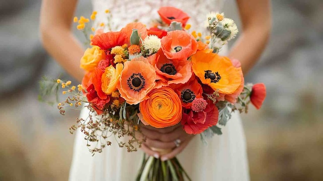 43 Country Wedding Ideas to Rustic Up Your Big Day 25 Bride holding a rustic bouquet of orange and red ranunculus and poppies, perfect for a vibrant country wedding theme