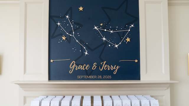 Navy constellation sign reading Grace and Jerry with September 28, 2025, displayed above a mantel lined with rows of white escort cards.