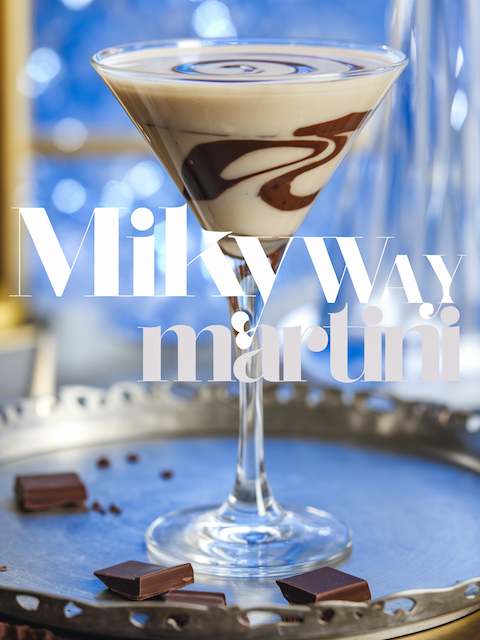 Milky Way Martini with creamy swirl and chocolate ribbons in a martini glass, blue bokeh backdrop, celestial wedding cocktail.