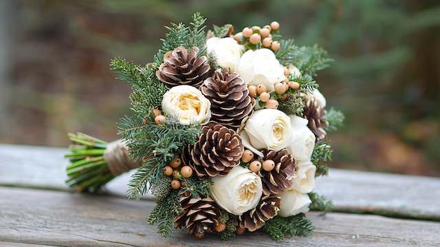 Pine Cone Bridal Bouquet Winter bridal bouquet with white roses, pine cones, evergreen branches, and beige berries for a rustic woodland wedding look