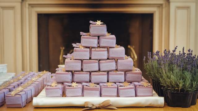 Pyramid of lavender soap wedding favors with gold star tags, displayed on satin tray beside potted lavender, celestial theme.