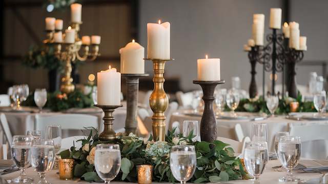 Candlestick Clusters Rustic wedding table with clustered candlesticks in mixed metal finishes surrounded by greenery, creating a warm and elegant candlelit centerpiece.