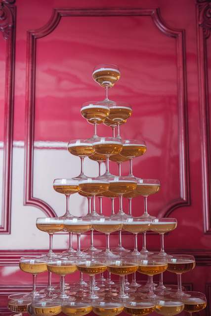 Champagne Tower A champagne tower made of coupe glasses against a vibrant pink wall, showcasing an elegant and celebratory display.