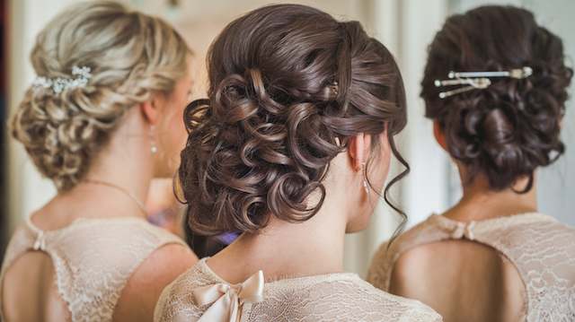 Curled Updo Three bridesmaids with curled updos and lace dresses seen from behind, featuring soft pinned curls and delicate hair accessories.