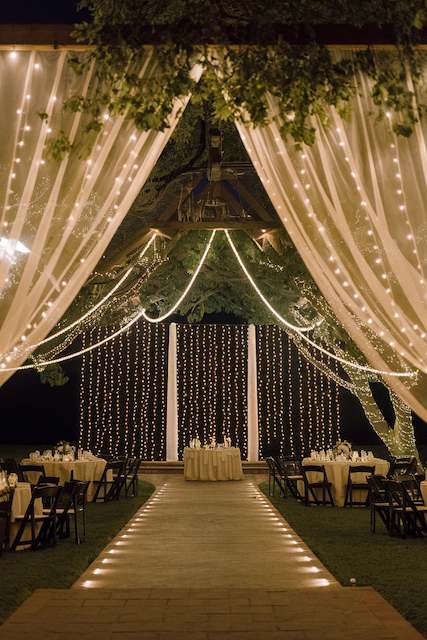 Curtain String Lights Outdoor wedding venue draped with sheer fabric and cascading curtain string lights, creating a warm glowing canopy above tables and chairs.