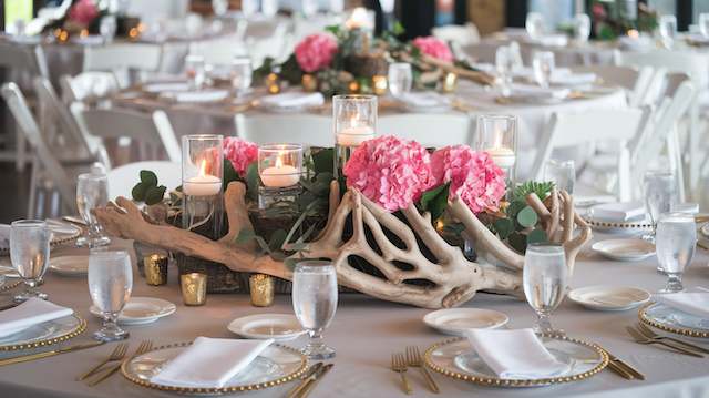 Driftwood Accents Rustic wedding table with driftwood centerpieces, pink hydrangeas, and floating candles surrounded by elegant place settings and glassware.