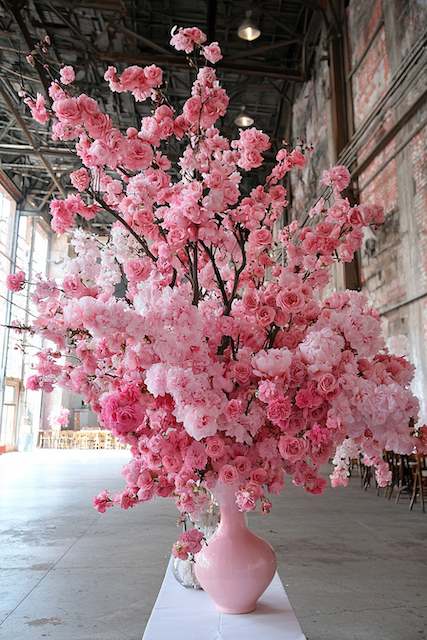 Indoor Wedding Reception A grand display of pink and white cherry blossoms in a tall vase, adding a vibrant and lush touch to an industrial-style venue.