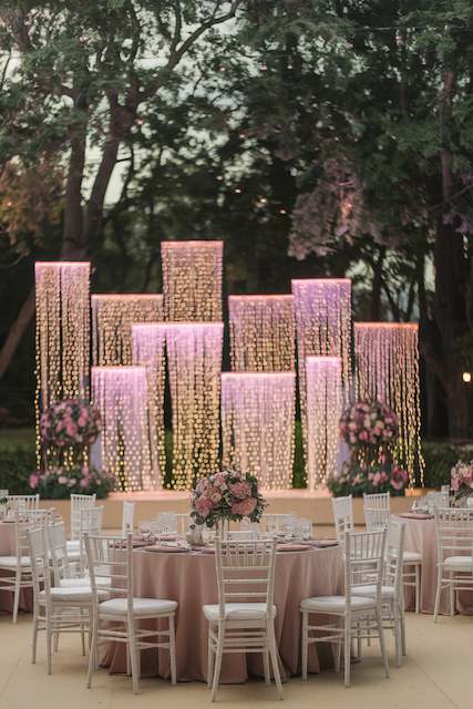 LED Waterfall Lights LED waterfall lights with cascading warm light create a stunning backdrop at an outdoor wedding reception, surrounded by trees.