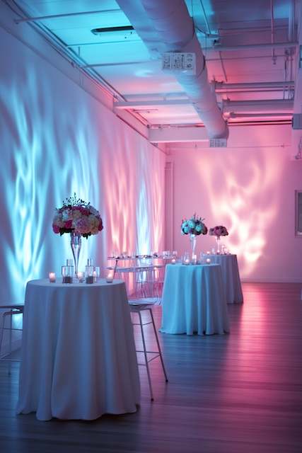 Mood-Enhancing LED Lighting A contemporary event space with tables featuring pink and white floral arrangements, illuminated by blue and pink uplighting for a vibrant atmosphere.
