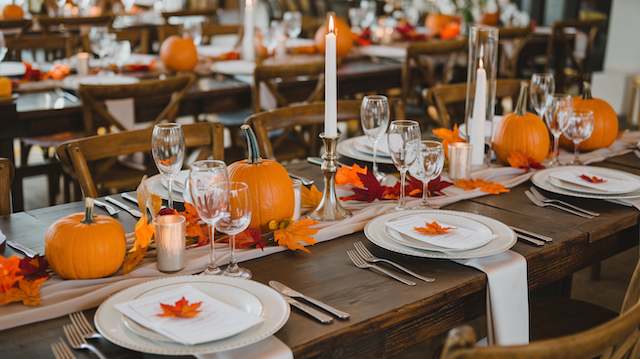 Fall wedding tablescape with mini pumpkins, orange leaves, candles, and rustic wooden seating creating a warm harvest-inspired centerpiece. Orange Accents for Fall Weddings