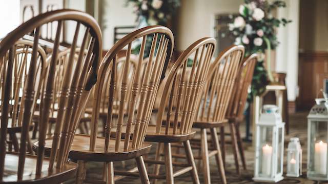 Windsor Chairs Rows of Windsor chairs with rounded backs and vertical spindles, set indoors next to lanterns and floral arrangements for a rustic wedding.