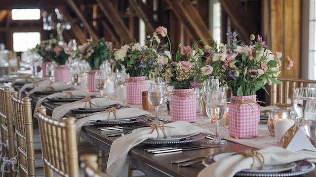 Wedding Decor 25 Pink gingham-wrapped jars filled with wildflower centerpieces on a rustic wedding tablescape with glassware and layered place settings