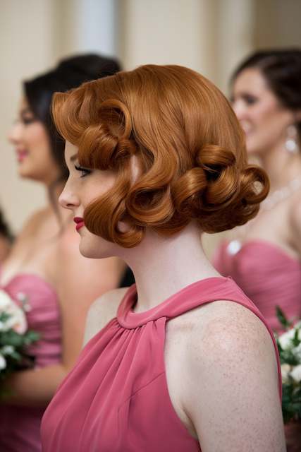 Curly Faux Bob Bridesmaid with a curled faux bob styled in soft vintage curls wearing a pink dress, shown in profile with other bridesmaids in the background.