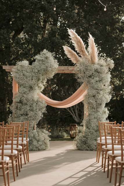 Delicate Wooden Arches Wrapped in Baby’s Breath A romantic wedding ceremony arch adorned with lush baby’s breath and dramatic pampas grass, creating a stunning natural backdrop for the vows