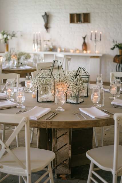 Glass Terrariums with Suspended Baby’s Breath Charming wedding table with modern glass lanterns filled with baby’s breath and glowing candles, surrounded by crystal-clear glassware and a soft eucalyptus garland, creating an elegant and intimate atmosphere