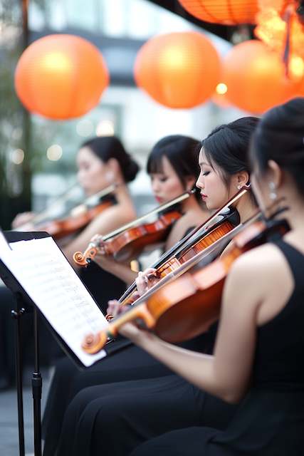 Live Ceremony Music String quartet of women in black dresses play violins at an outdoor wedding, focused on sheet music beneath glowing orange lanterns.