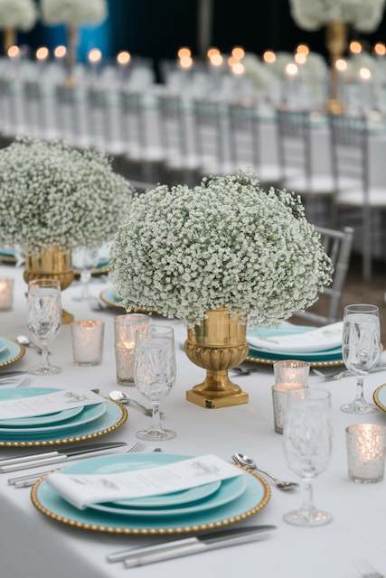 Minimalistic Arrangements of Baby’s Breath in Brass Vases Elegant wedding table featuring baby’s breath centerpieces in gold urns, set against soft teal plates, glassware, and candles for a sophisticated and romantic atmosphere