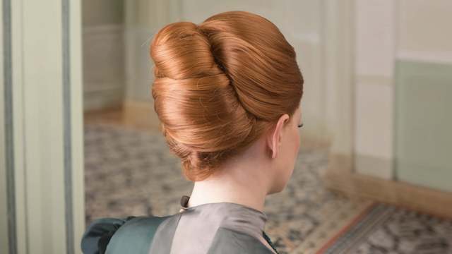 French Twist Hairstyle Elegant French twist updo on a red-haired bridesmaid, styled smoothly with structured volume, shown from the back in a formal setting.
