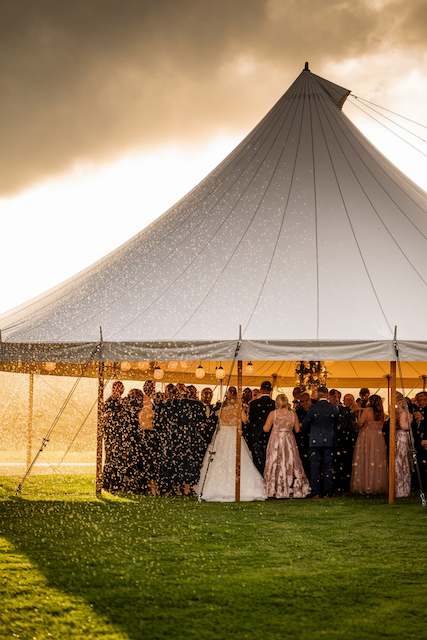 tent rental for bad weather Guests gather under a sailcloth wedding tent as rain falls at golden hour, a beautiful backup plan for an outdoor ceremony.