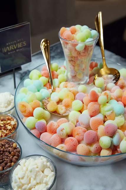 Alcoholic Dippin’ Dots Alcoholic dippin' dots in pastel colors, served in a large glass bowl and cup, with toppings like chopped nuts and chocolate pieces in surrounding bowls