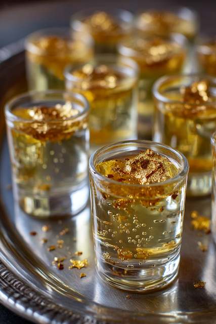 Champagne jello shots topped with edible gold leaf Champagne jello shots topped with edible gold leaf, served in small glass cups on a silver platter, with bubbles rising through the liquid