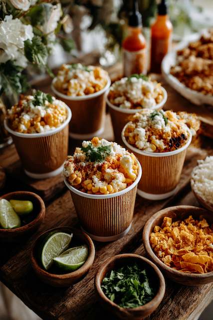 Elote Cup Station (Mexican Street Corn in Disposable Cups) Delicious Mexican street corn served in disposable cups with toppings like cheese, chili powder, and fresh cilantro, accompanied by lime wedges