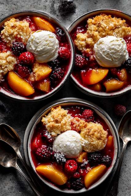 Fruit Cobblers Individual servings of fruit cobbler with a golden crumble topping and a scoop of vanilla ice cream, served in rustic bowls