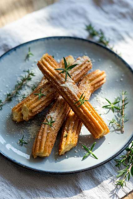 Savory churro fries dusted with parmesan and herbs Golden savory churro fries dusted with parmesan and fresh herbs, served on a rustic plate — a creative late-night wedding snack twist on the classic sweet treat.